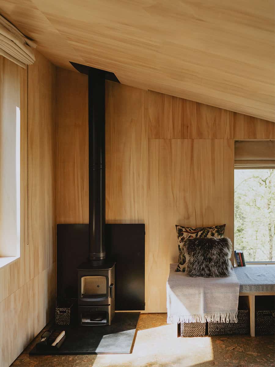 Elmore Treehouses interior detail showing wood-burning stove and window seat in plywood-lined room